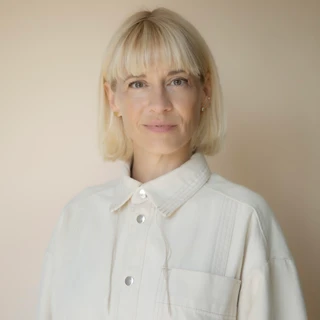 Portræt af en blond kvinde med kort hår, iført en lys jakke med knapper, set mod en neutral beige baggrund. (Marie Høst)